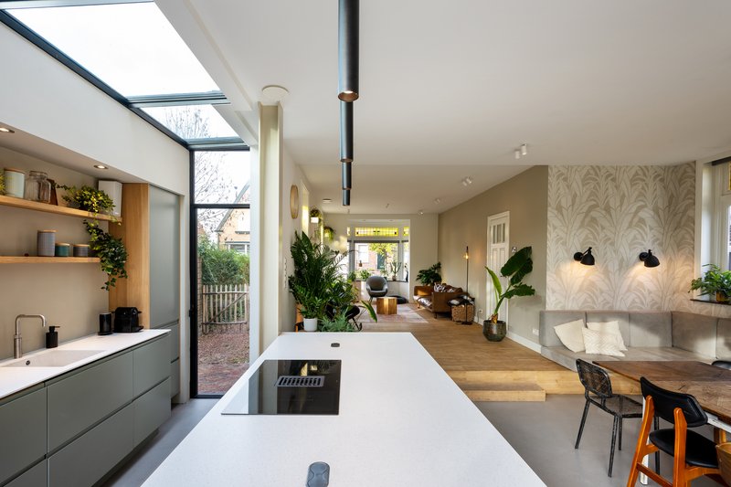 White kitchen island with integrated hob opening onto the dining area with wallpapered feature wall