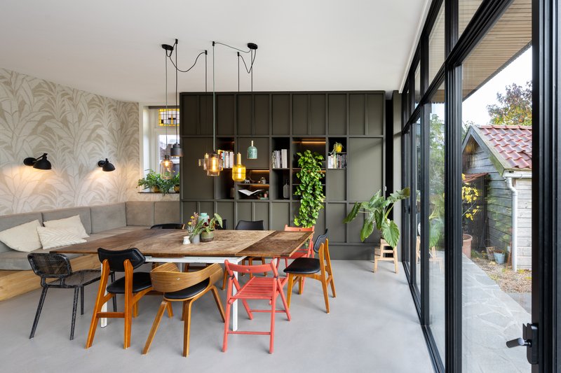 Dining table with mismatched chairs beside full-height glazing and a grid storage wall
