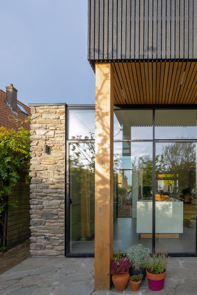 Glazed corner entry with timber column catching afternoon sunlight and potted plants below