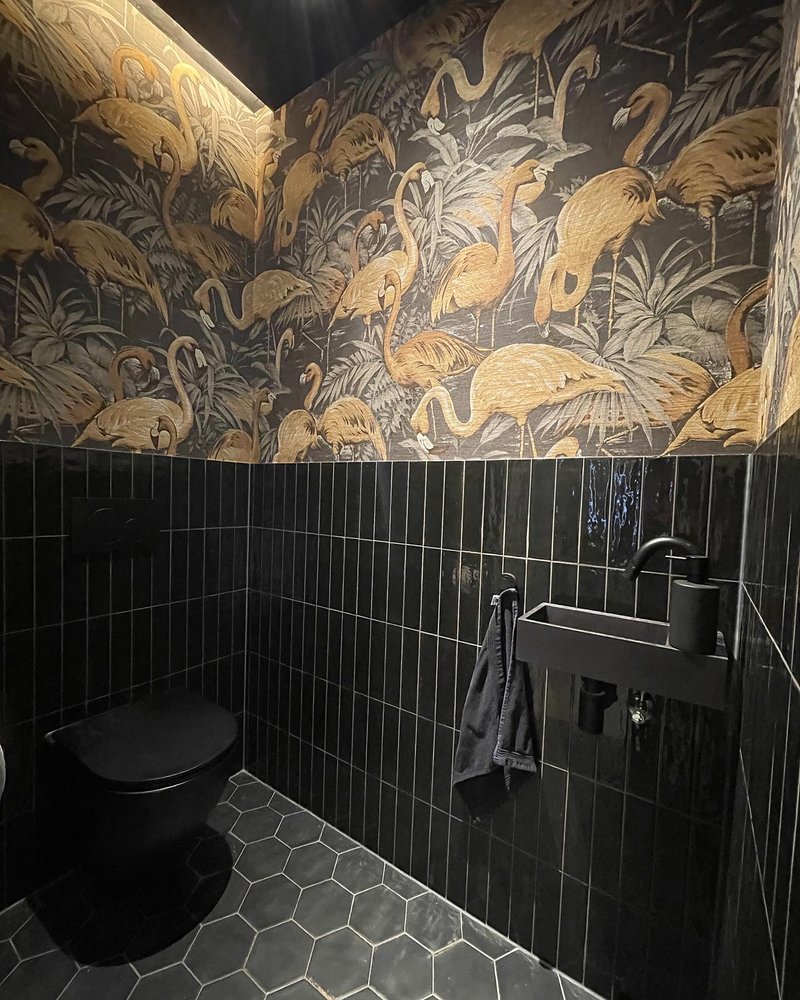 Powder room with black vertical tile wainscoting beneath a gold flamingo-patterned wallpaper mural