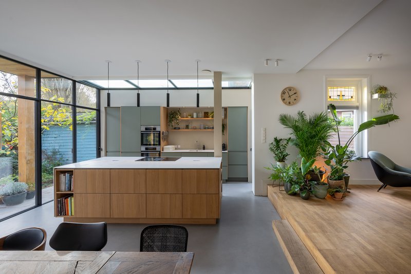 Kitchen island with timber base and pendant lighting viewed from dining table toward garden through glazed doors
