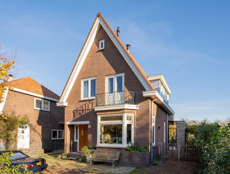 Street facade showing the steeply pitched brick gable with white trim under a clear blue sky