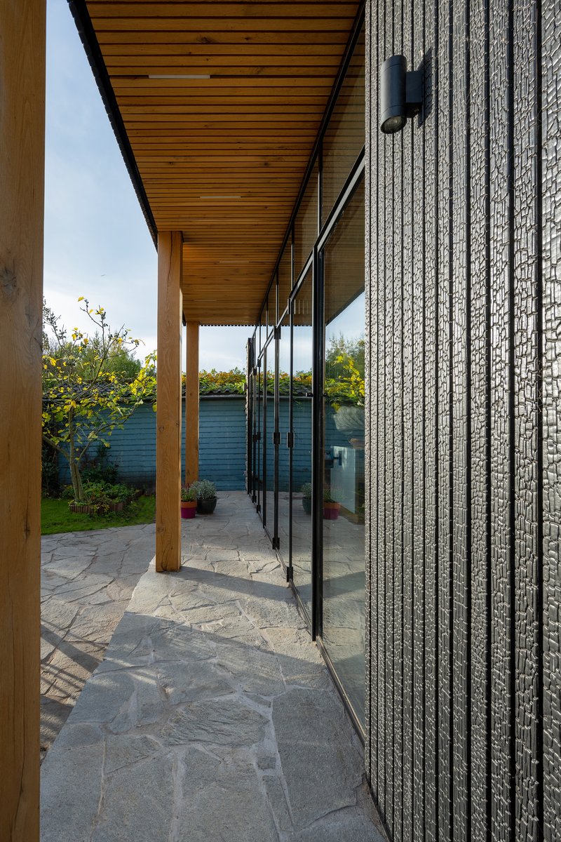 Covered terrace with timber posts and ceiling alongside textured brick wall and floor-to-ceiling glazing
