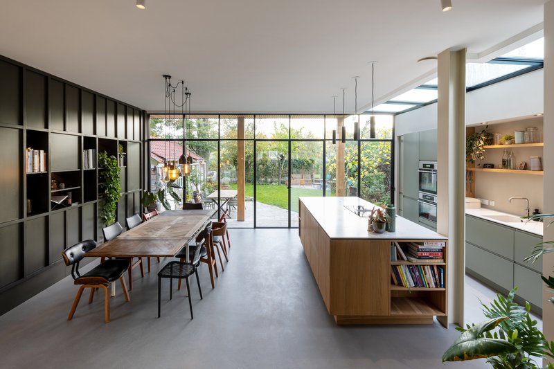 Open kitchen and dining area with timber island, black shelving wall, and full-height glazing to garden