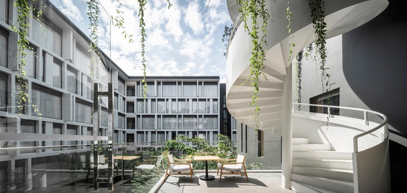 Interior courtyard with white spiral stair and cascading vines under open sky