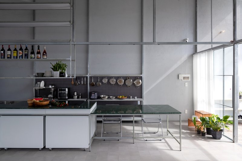 Kitchen with green glass dining table and steel shelving displaying cookware beneath afternoon sunlight