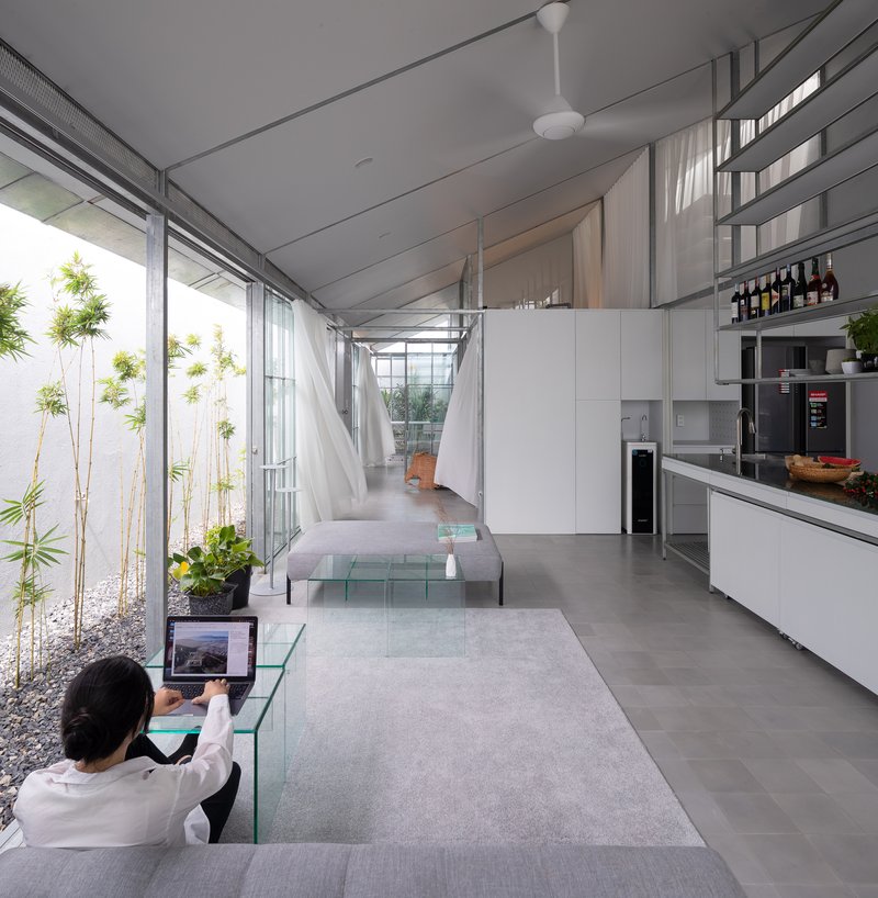 Living area with glass coffee tables and person seated in chair overlooking planted courtyard