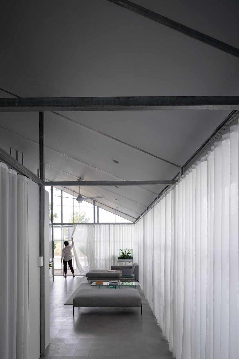 Interior corridor with exposed steel frame and white curtains flanking a figure at the window