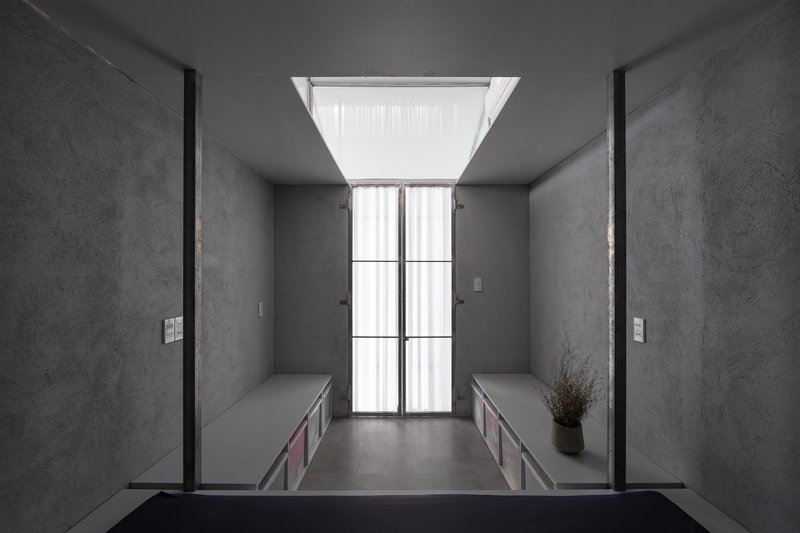 Narrow corridor framed by built-in benches with central skylight and black-tiled bathroom beyond