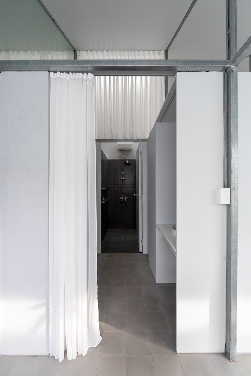 Passage with white curtain partially drawn revealing dark tiled shower enclosure under skylight