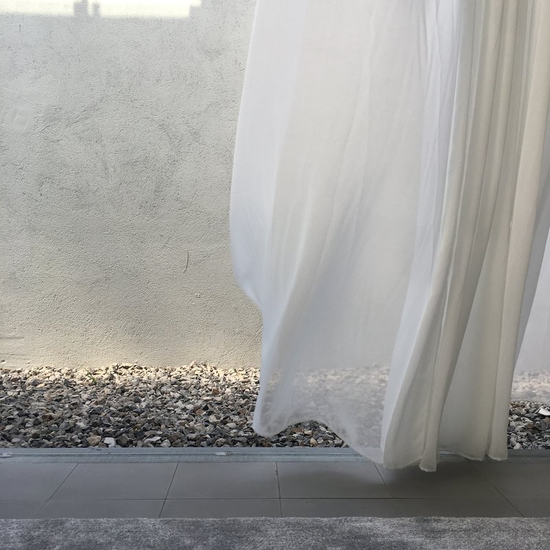 Detail of white curtain hem meeting gravel courtyard floor against textured plaster wall