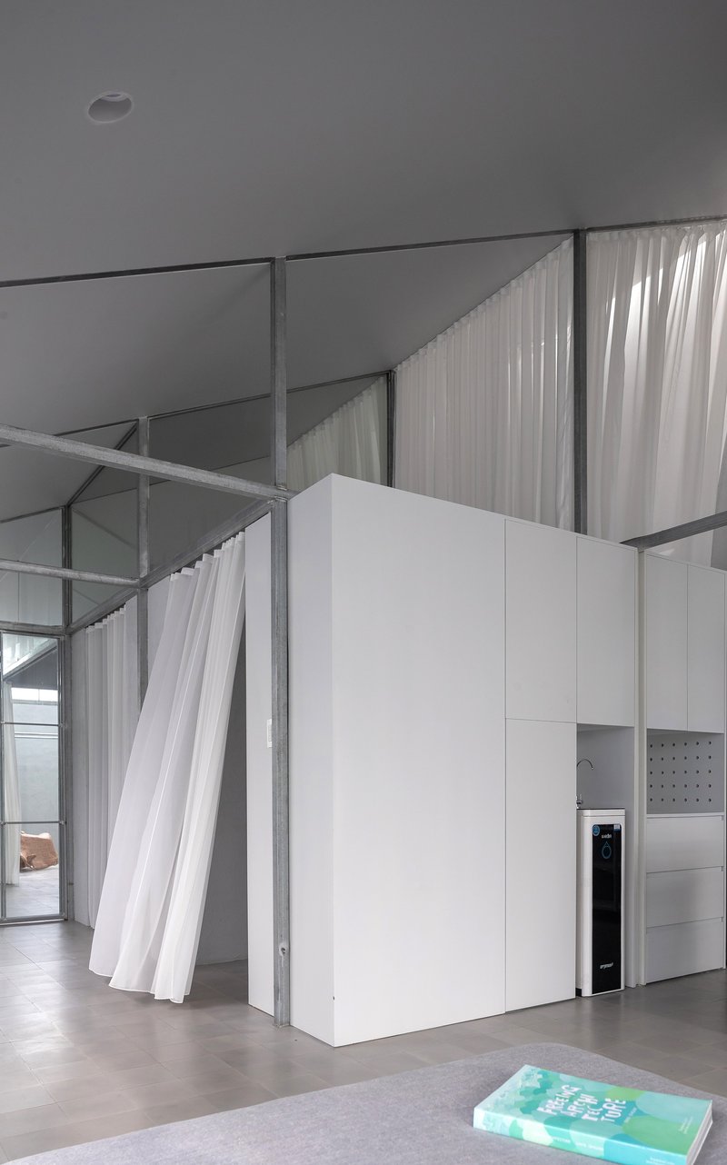 Freestanding white cabinet box with exposed steel framing and white curtains suspended from the ceiling structure