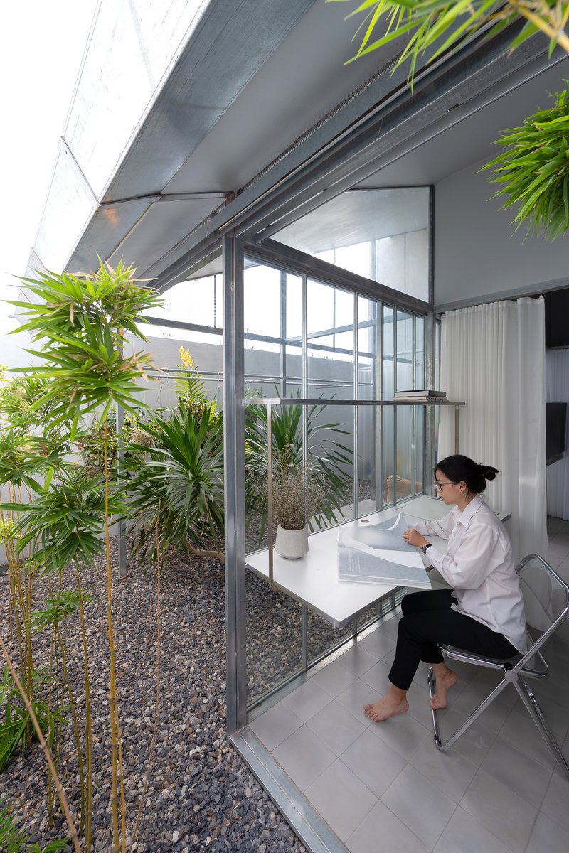 Narrow desk niche with a person seated beside a planted gravel bed enclosed by steel-framed glazing