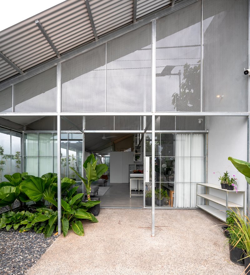 Entry threshold with perforated metal screens above glazed doors and planted beds with large tropical foliage