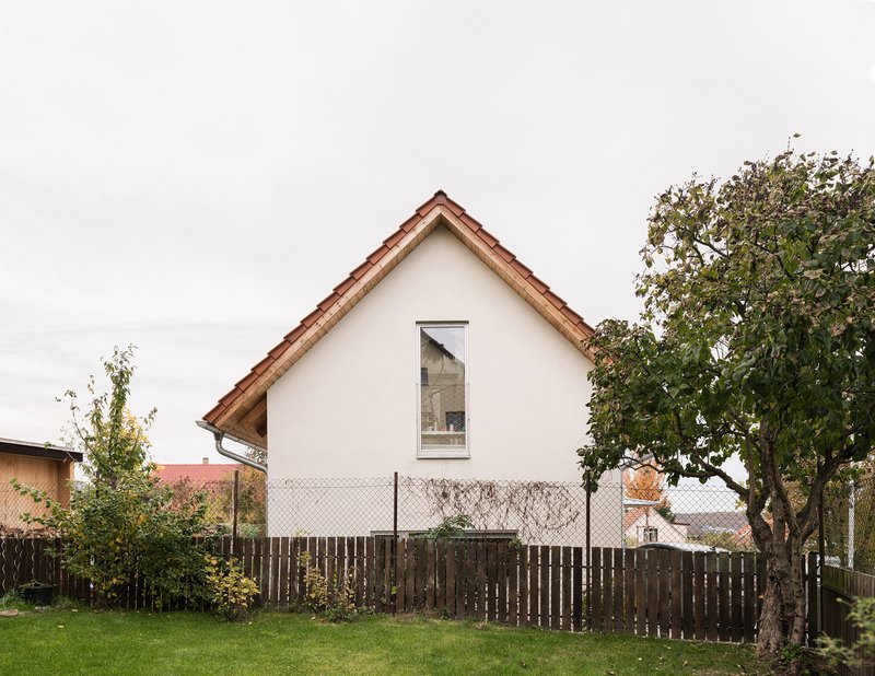 White rendered gable facade with single tall window viewed across lawn and weathered timber fence