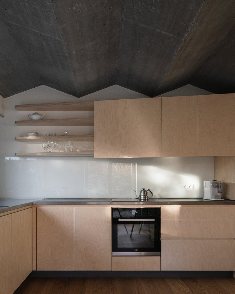 Light wood kitchen cabinetry with open shelving under a folded concrete ceiling catching afternoon sunlight