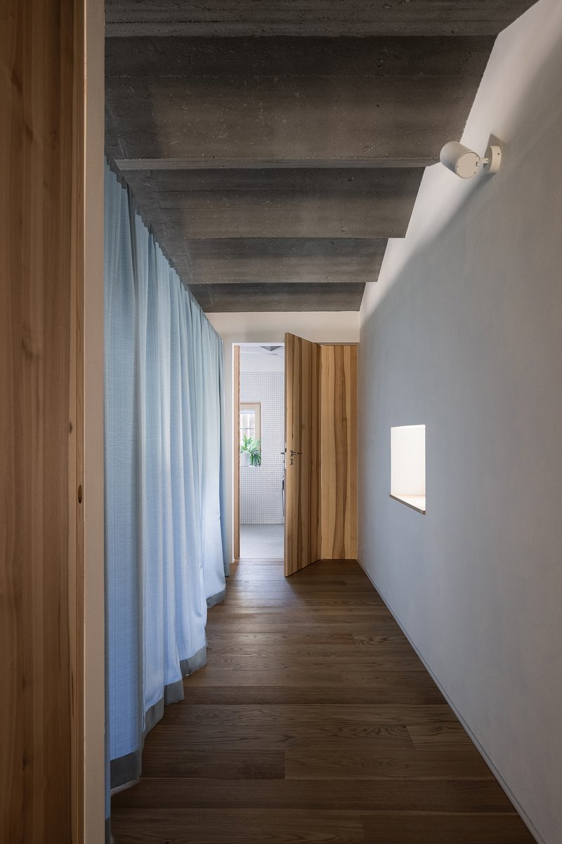Corridor with exposed concrete beam ceiling and floor-length blue linen curtain alongside recessed wall light