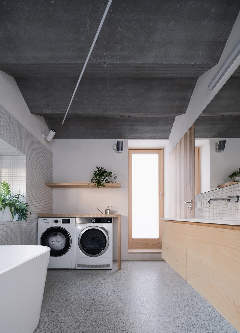 Bathroom with freestanding bathtub, front-loading washers and exposed concrete beam ceiling