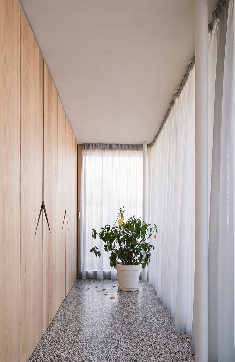 Narrow hallway with floor-to-ceiling timber cabinetry, terrazzo flooring and potted plant at curtained window