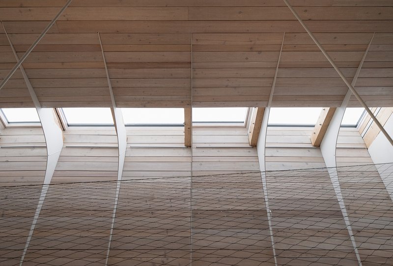Interior view of the timber-clad sloped ceiling with rhythmic steel tension rods and skylights above