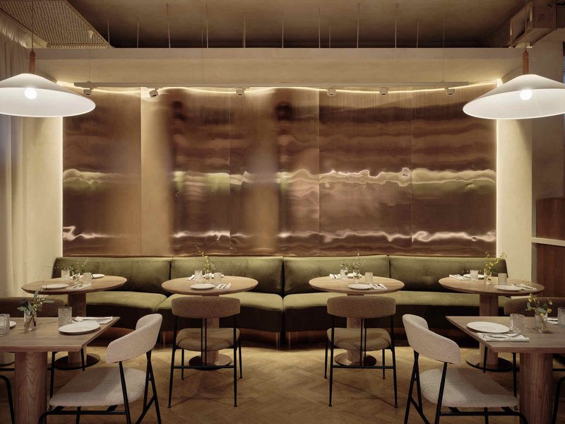 Banquette seating along translucent backlit wall panels with round tables and pendant lights overhead
