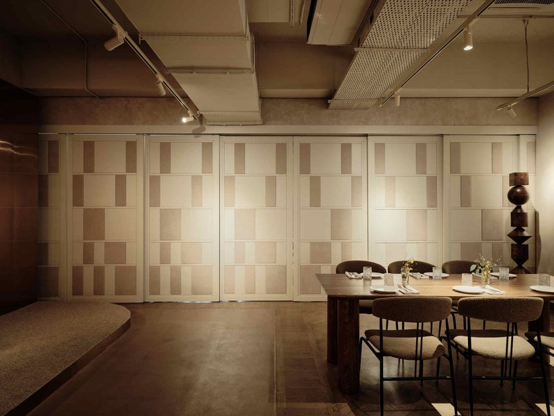 Folding panels with alternating wood tones beside a dining table and sculptural wooden floor lamp