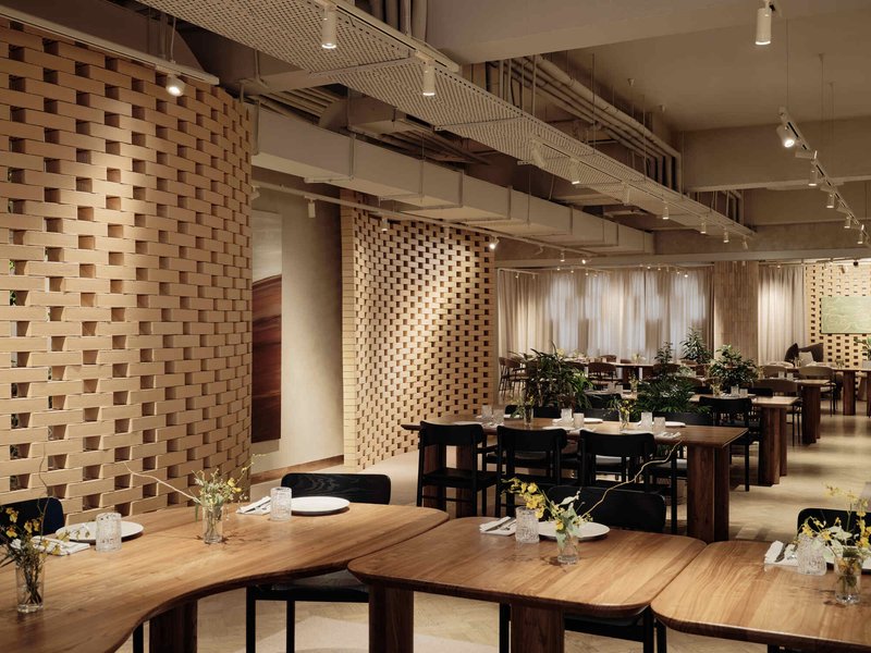 Dining space with perforated timber screens, exposed concrete ceiling beams, and track lighting overhead