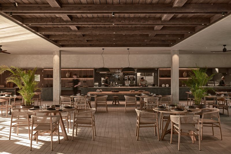 Dining area with timber tables and chairs beneath a recessed timber ceiling and open kitchen
