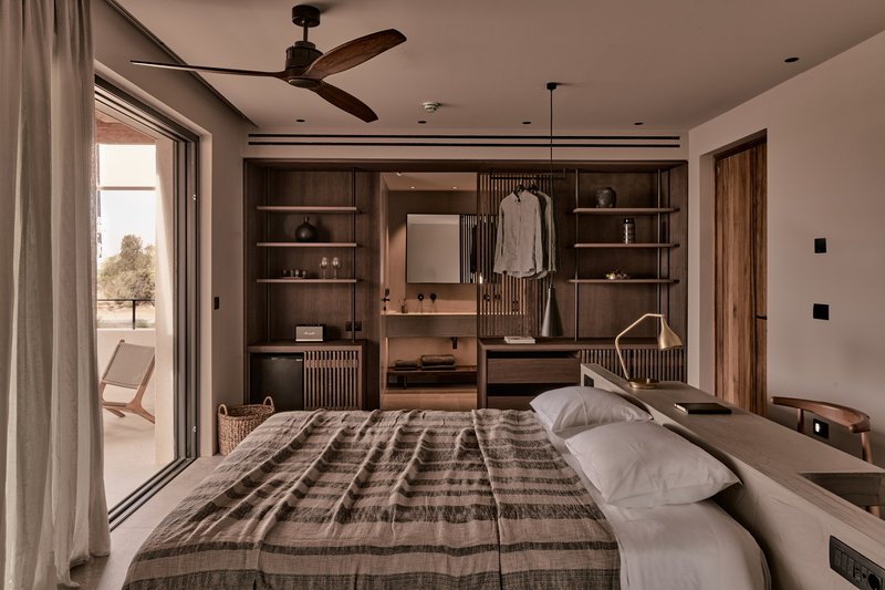 Bedroom with dark timber shelving unit and sliding glass doors opening to terrace with lone tree