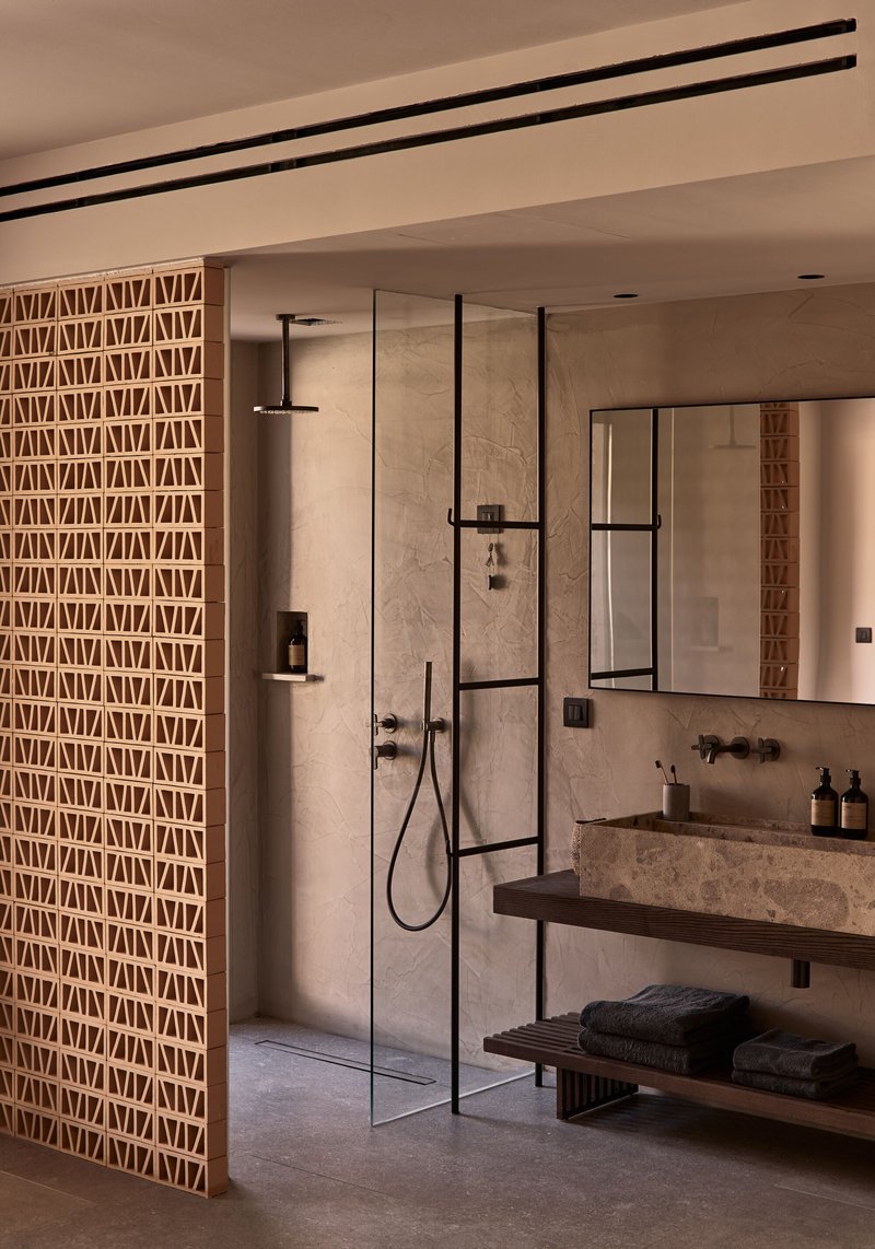 Bathroom with geometric lattice screen, frameless glass shower enclosure, and stone vanity beneath linear ceiling tracks