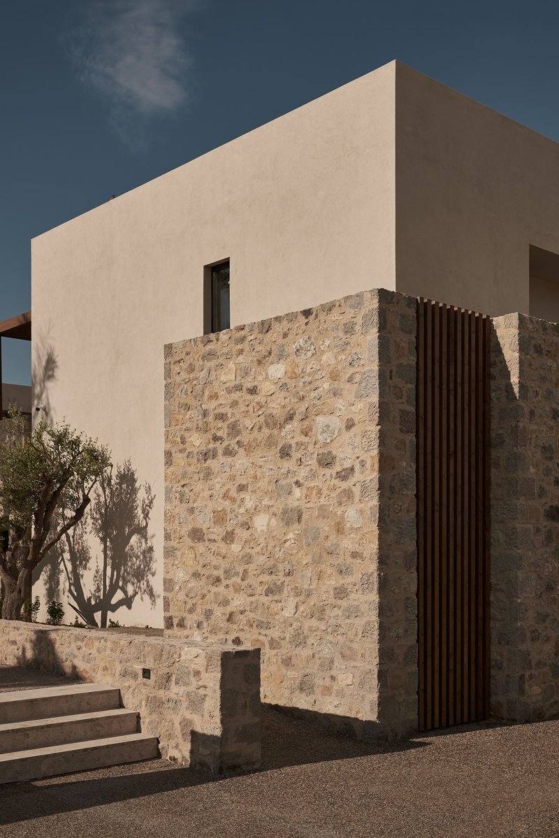 Corner facade combining pale stucco upper volume with rough stone lower wall and vertical timber screen