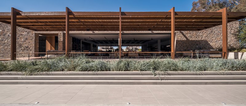Stone facade with timber pergola and deep overhang fronting a planted bed of grasses