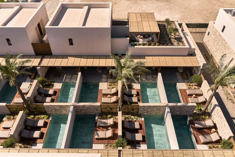Aerial view of courtyard pools with timber decking and palm trees between white stucco volumes