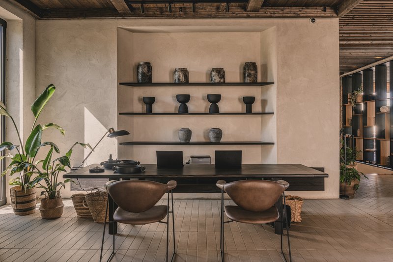 Dining area with black shelving displaying ceramics against a plastered wall beneath an exposed timber beam ceiling