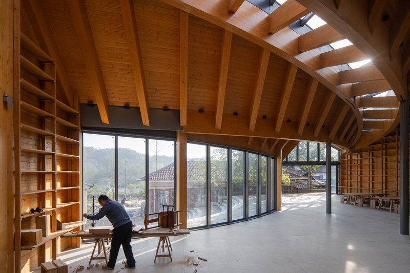Interior with exposed timber beams, barrel-vaulted ceiling with skylights, and full-height windows overlooking hills