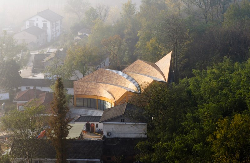 Elevated view of the three-lobed timber roof emerging from the hillside village in morning fog