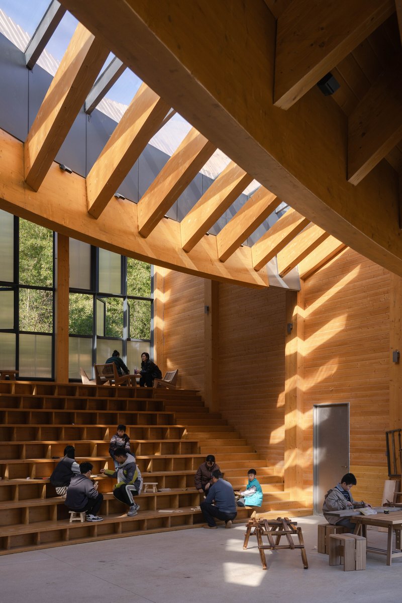 Stepped timber seating with visitors gathered below exposed wood beams and tall glazed walls in afternoon light