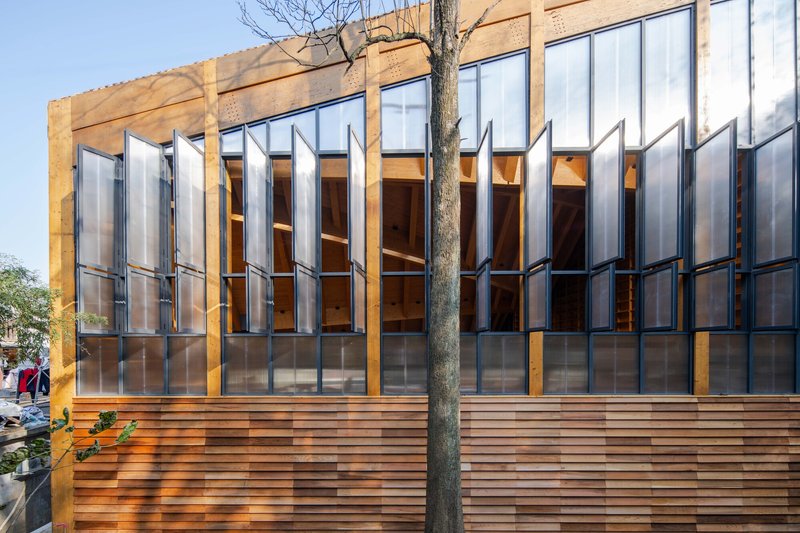 Exterior facade with vertical metal shutters above horizontal timber cladding and a bare tree in front