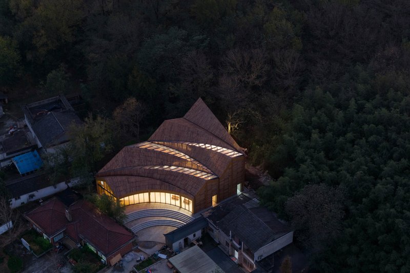 Aerial view of the three-lobed shingled roof with illuminated skylights at night
