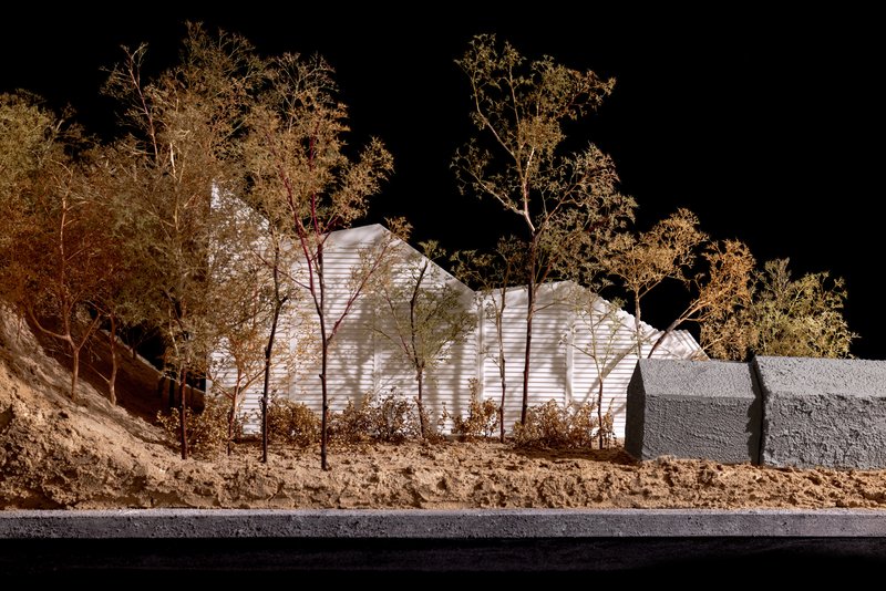 Side view of illuminated physical model with corrugated white facade set against bare trees at night