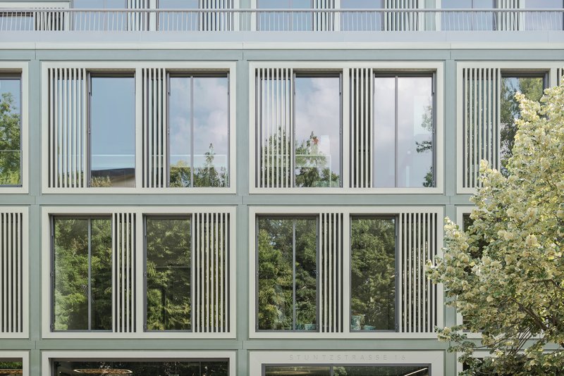 Close-up of the facade showing vertical slat screens flanking large glazed panels that reflect surrounding foliage