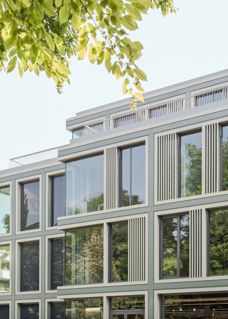 Upper floors of the facade with recessed terrace behind vertical screening and overhanging tree branches