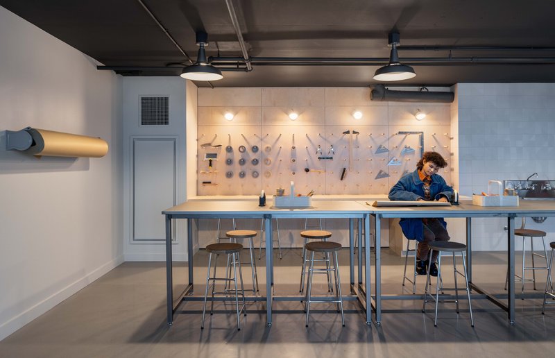 Workshop space with tool wall and high metal tables where a person sits under pendant lights