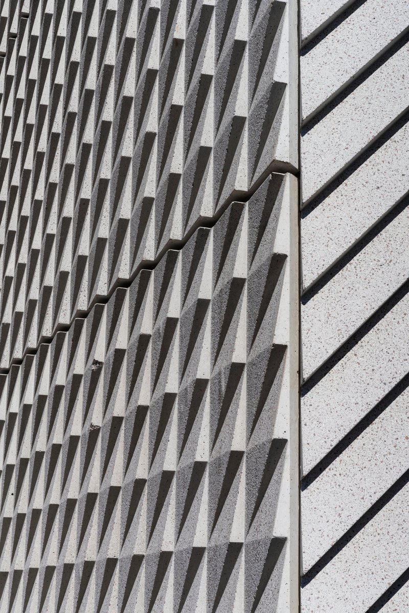 Close-up of textured concrete wall with protruding vertical fins meeting a smooth terrazzo surface