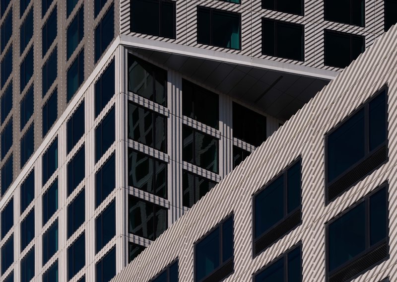 Facade detail showing recessed balcony framed by diagonal striped cladding and dark glazing
