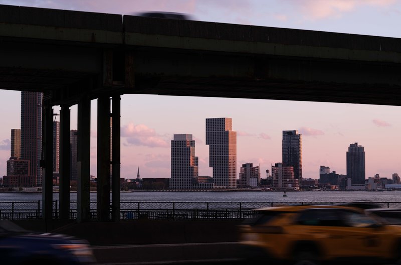 View beneath an elevated highway of the stepped towers across the water at dusk with a taxi passing