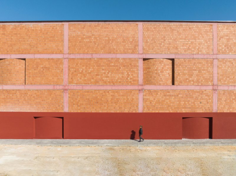 Facade with two doorways in red plaster base below upper terracotta brick wall as figure walks past