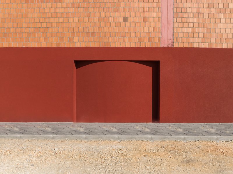 Arched doorway recessed into the red plaster wall above a patterned stone paving strip