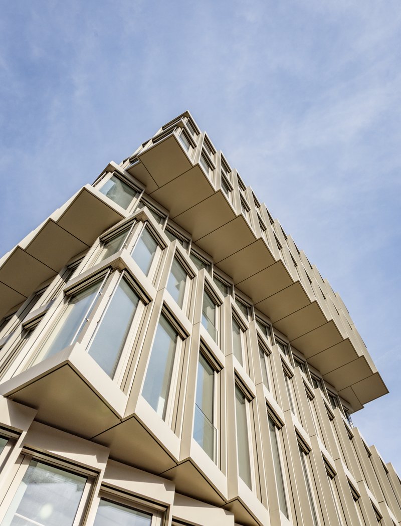 Upward view of cantilevered corner with protruding window bays and deep recessed soffits against blue sky