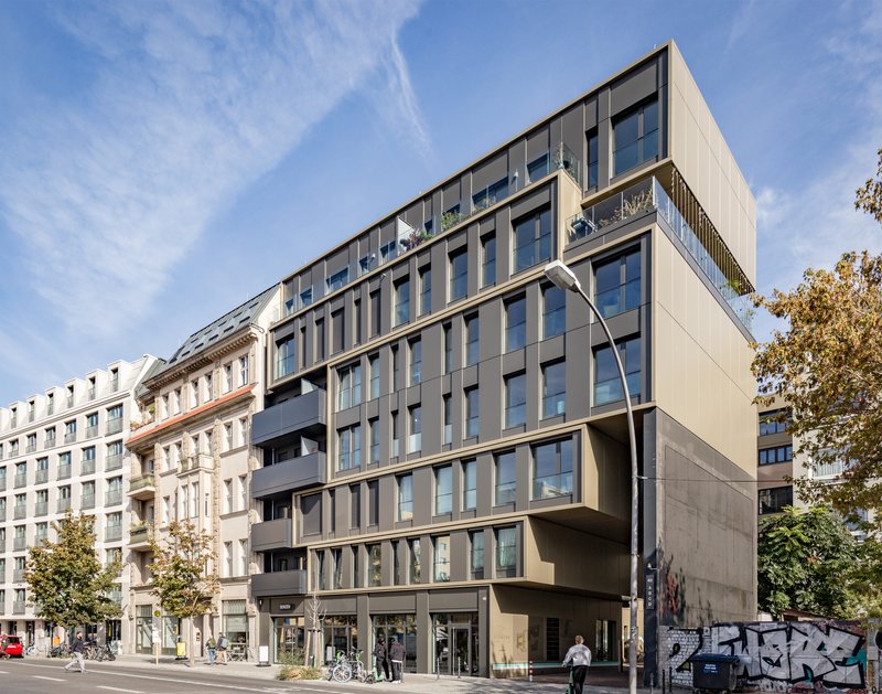 Street facade showing cantilevered volumes above ground-level retail with pedestrians and bicycles passing by